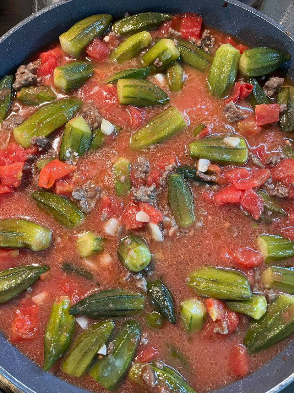 Бамия с томатами в сковороде: стручки плавают в густом томатном соусе с кусочками помидоров, соус начинает густеть и обволакивать овощи.