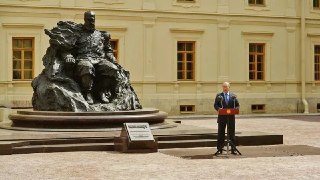 Скульптура на постаменте у фасада Гатчинского дворца; в кадре — трибуна и выступающий человек во время церемонии открытия.