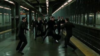 Группа людей в формальной одежде дерётся на платформе метро; много тел и сложная сцена с взаимодействием персонажей в движении.