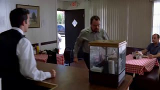 Мужчина в кафе/баре резко шагает к прилавку рядом с кассовым аппаратом и витриной, кадр с бытовым действием и экспрессией.