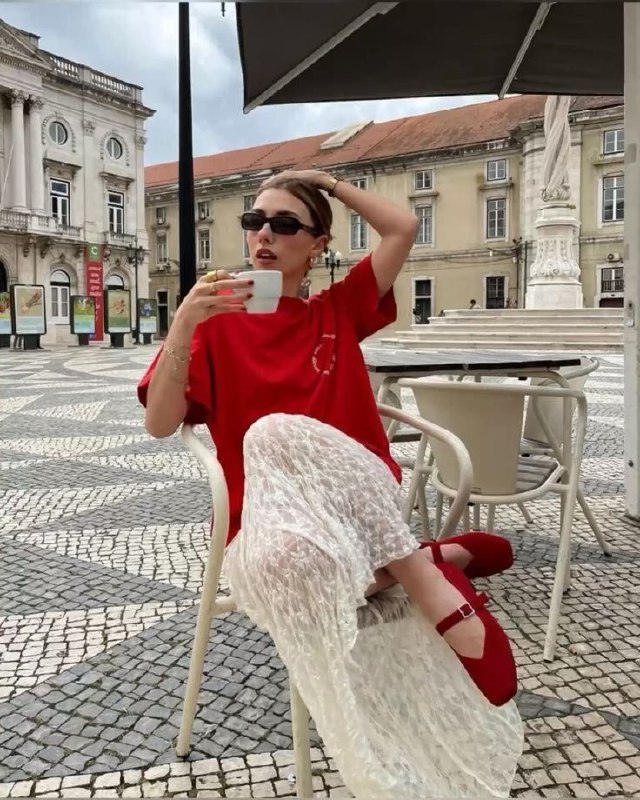Женщина в красной футболке и белой кружевной юбке сидит в уличном кафе с чашкой, сочетание яркого красного и лёгкой белой текстуры в повседневном образе.