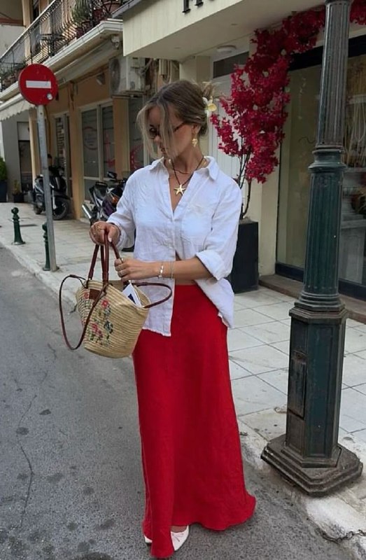 Образ с белой рубашкой и красной юбкой, плетёная сумка и спокойный городской фон — пример баланса чистой базы и яркого акцента в комплекте.