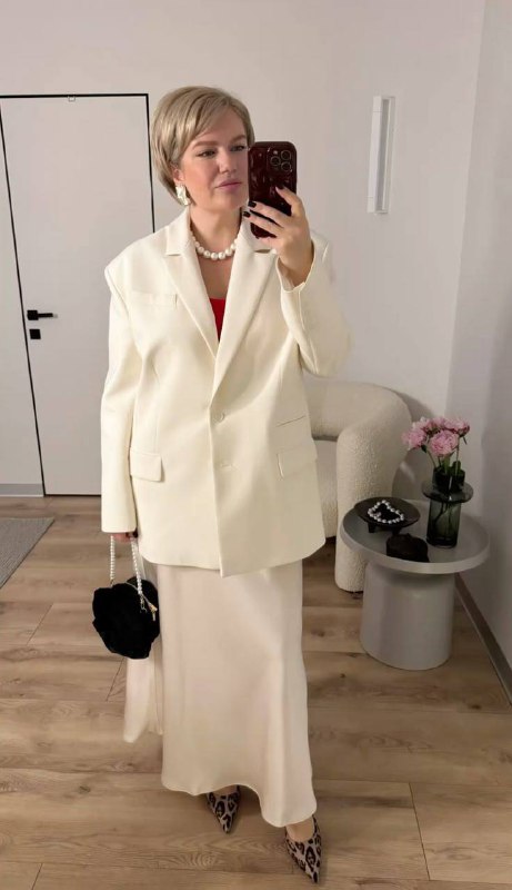 Женщина в кремовом жакете и длинной светлой юбке в интерьере; мягкий нейтральный комплект, подходящий для праздничного, но спокойного образа.