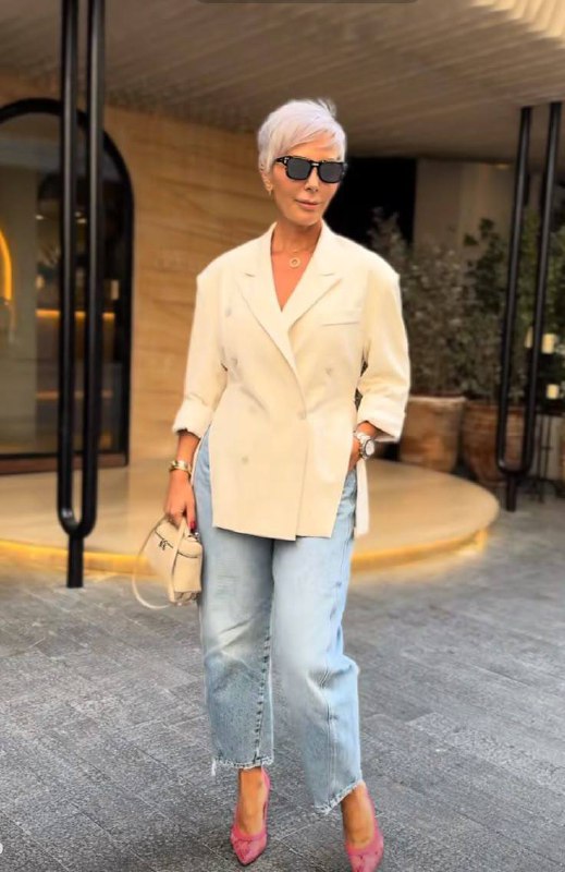 Женщина в кремовом жакете и светлых джинсах с яркими туфлями; сочетание повседневного и нарядного, уместное для тёплой погоды и неформального торжества.