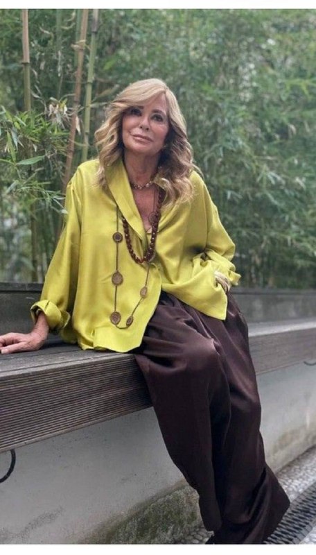 Женщина на скамейке в яркой лимонно‑зелёной блузе и тёмных брюках; смелый цветовой акцент уместен для тех, кто хочет выразить энергию.