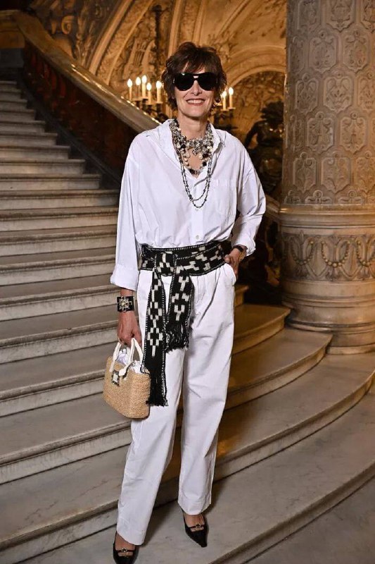 Женщина в белом костюме с крупными аксессуарами в классическом интерьере; образ с контрастными деталями и текстурами для торжества.