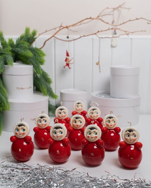 Несколько небольших красных неваляшек на праздничном столе рядом с декором и еловой веткой; композиция подчёркивает тематический тренд и коллекционирование.