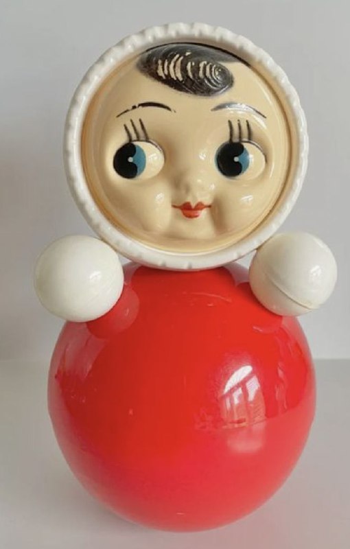 Макро‑съёмка лицевой части винтажной неваляшки: крупные глаза и округлая форма, детализация фарфоро‑пластиковой текстуры игрушки.