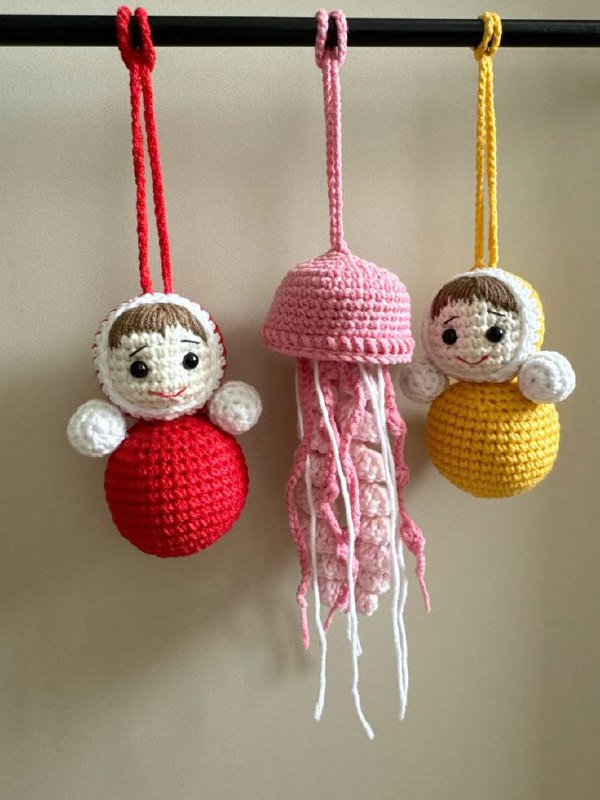 Рукодельные вязаные брелоки‑неваляшки разного цвета, висящие на крючках; текстурный кадр, подчёркивающий ремесленный и хэндмейд аспект тренда.