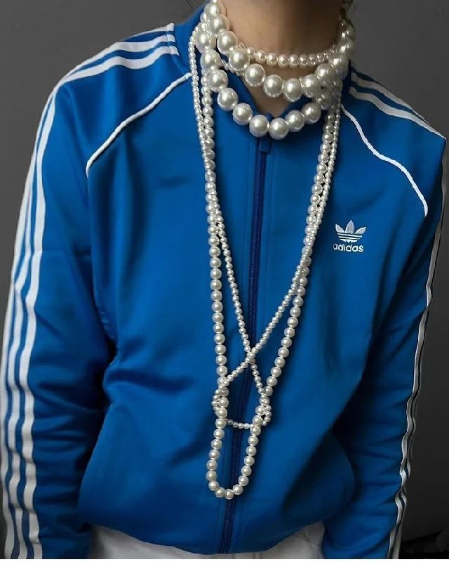 Ближе: синяя спортивная куртка adidas, поверх — несколько нитей жемчуга разной длины, демонстрирующие смешение стилей.