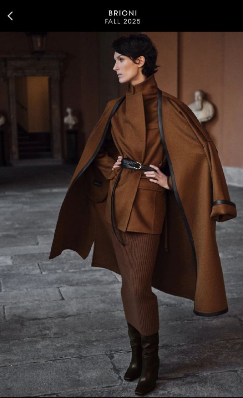 Модель в глубоком тёплом коричневом пальто и костюме на улице исторического интерьера — элегантный образ с акцентом на структуру ткани.
