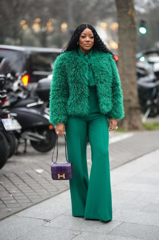 Женщина в насыщенном зелёном пушистом пальто и широких брюках на городском фоне — пример яркого модного зелёного в уличном стиле.