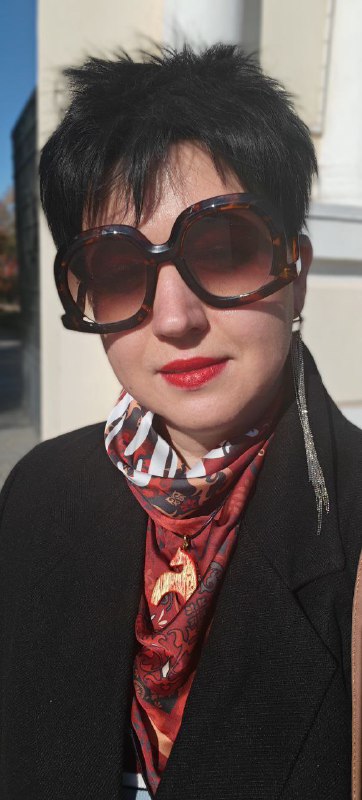 Уличное фото: женщина в солнечных очках и платке на шее, повседневный городской стиль с акцентом на узор платка, цвет помады и индивидуальность образа