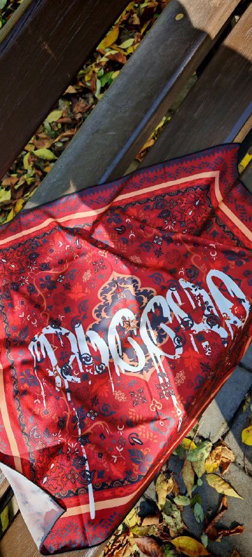 Платок, разложенный на осенних листьях: яркий красный платок с узором, вид аксессуара в деталях, текстура ткани и тёплый сезонный фон