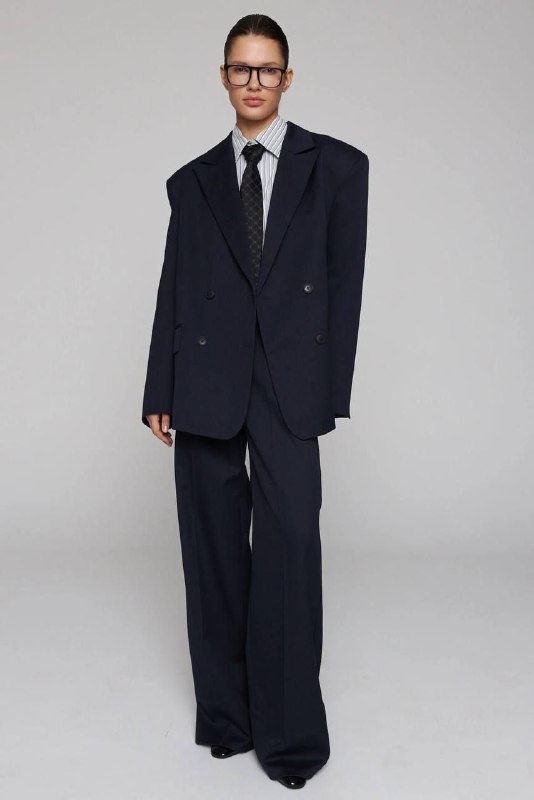 Модель в свободном двубортном тёмном костюме с широкими плечами — пример силуэта, подчёркивающего проявленность и силу формы.