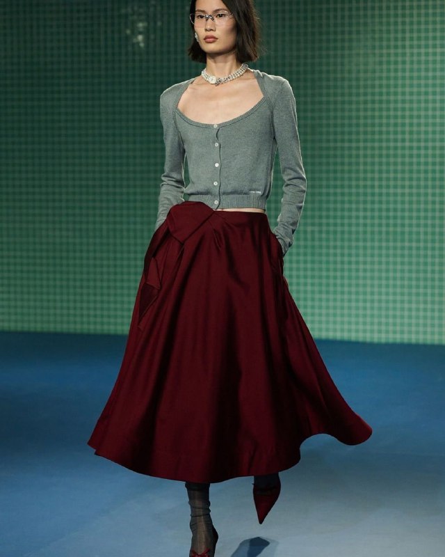 Женская модель в изумрудном кардигане и бордовой юбке — сочетание округлых форм и плавных линий, выражение мягкой и творческой энергии.