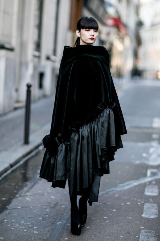 Чёрный драматичный плащ со складками и объёмом на городской улице — сочетание тяжести, масштаба и выразительной формы в образе.