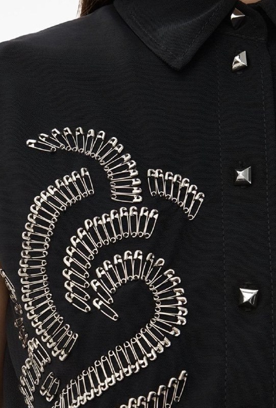 Деталь тёмной куртки, украшенной множеством серебряных булавок, выложенных декоративным узором — акцент на композиции и контрасте с тканью.