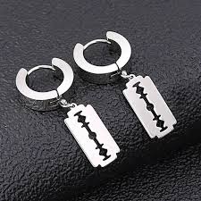 Пара серьг с подвесками в форме бритвенных лезвий на тёмном фоне: макросъёмка подчёркивает контуры, отражения и грубую эстетическую форму аксессуаров.