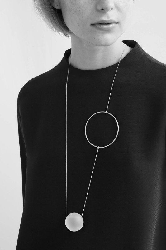 Монохромный образ с длинной подвеской: круг и шар на тёмном джемпере; иллюстрация того, как геометрия украшений передаёт настроение и контактность.