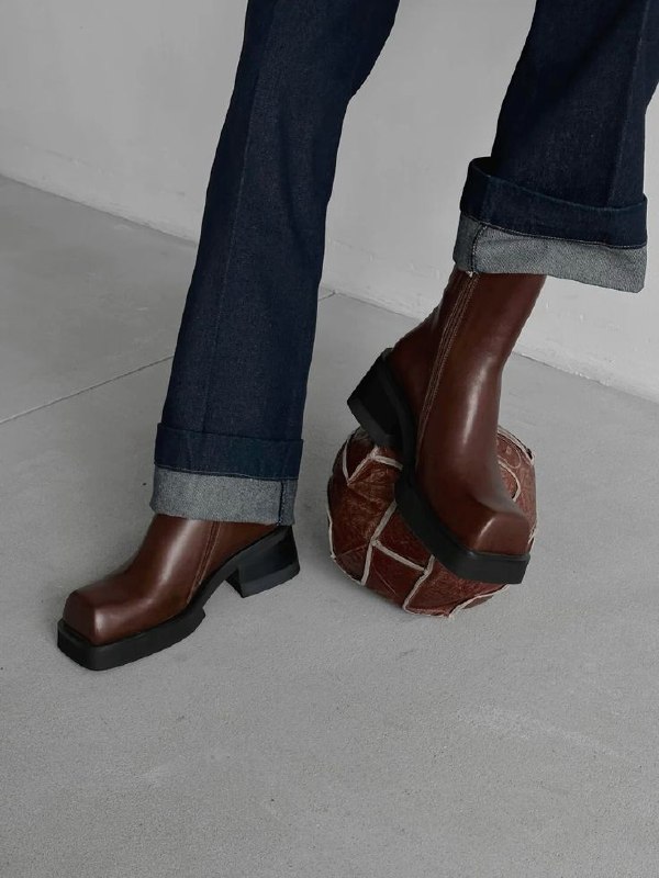 Коричневые ботинки на массивной подошве в движении, снятые снизу; фотография подчёркивает динамику шага и силу формы как акцента в образе.