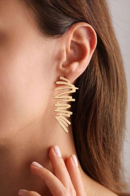 Крупный золотой асимметричный серьга на ухе крупным планом; игривая и ломанная форма как выражение свободы, дерзости и импульса в стиле.