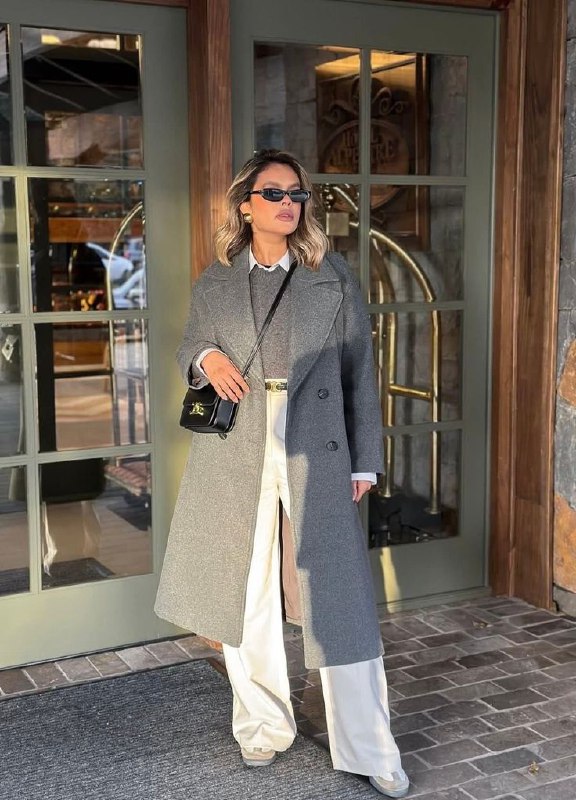 Женщина в сером пальто, светлые брюки и небольшой чёрный клатч — баланс серого с аксессуарами для завершённого образа.