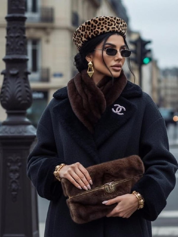 Элегантный образ с тёмной верхней одеждой и коричневой меховой отделкой, сумка и аксессуары подчёркивают фактуру и зону лица.