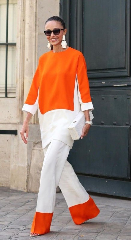 Женский образ с ярким оранжевым верхом и светлыми брюками — контраст оранжевого и белого/кремового для мягкого, чистого звучания.