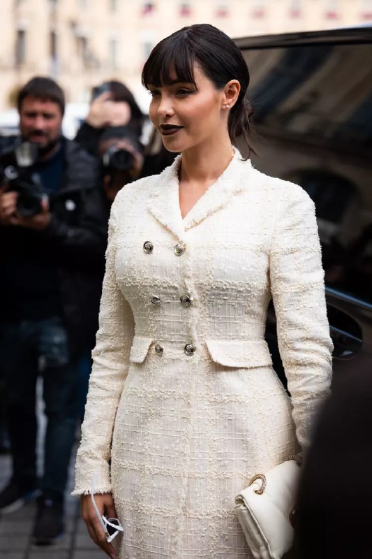 Женщина в белом твидовом пальто-двубортном жакете на фоне папарацци; классический элегантный образ в уличной среде, акцент на текстуру ткани.