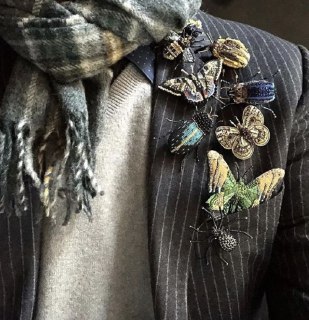 Крупный план пальто с декоративными брошь-элементами в виде бабочек и текстур, пример асимметричного и декоративного использования аксессуаров в образе.