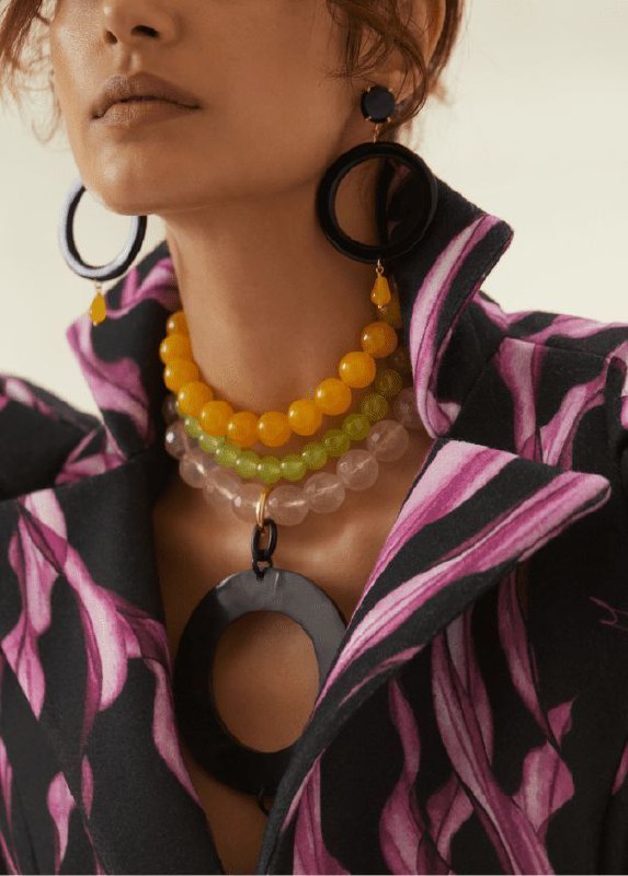 Модель в крупными колье из пластика и бус, сочетание ярких бижутерных форм и контрастных цветов, показывающее повтор масштаба и силуэта в аксессуарах.