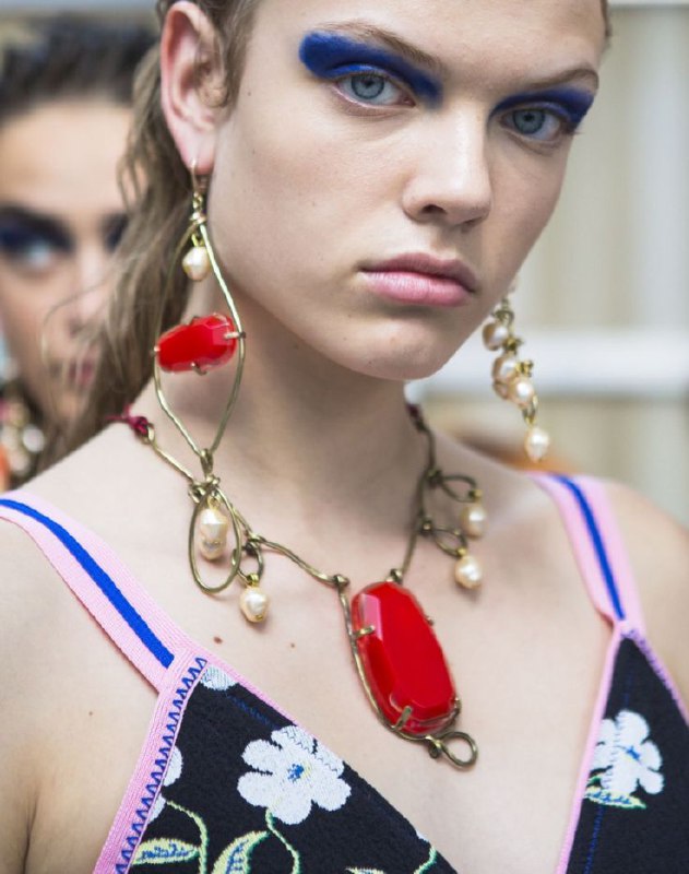 Подиумный кадр с моделью в крупном ожерелье с красной вставкой и подвесками, пример как одна яркая деталь становится главным акцентом в составе аксессуаров.