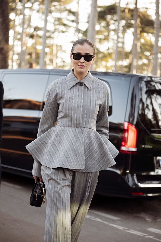 Уличный стритстайл: женщина в костюме с выраженной баской в полоску, подчеркнутый низ талии и архитектурный силуэт пиджака, городская сцена.