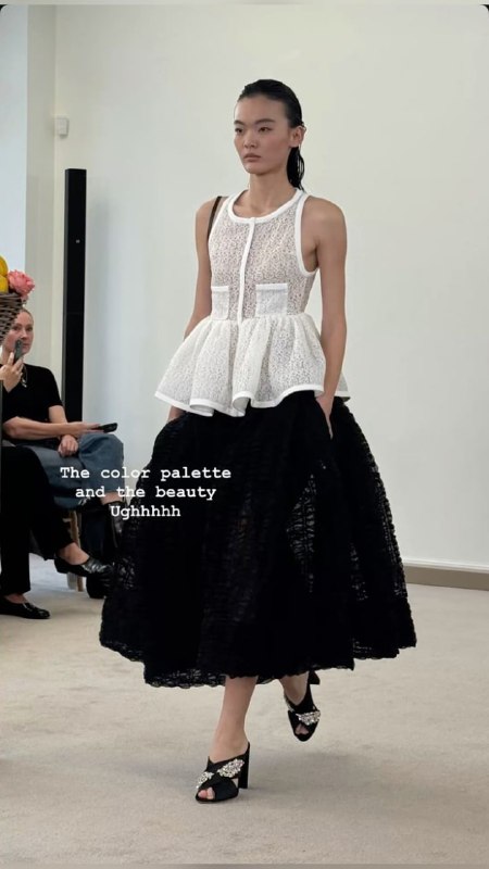 Подиумный кадр: модель в белой корсетной баске поверх чёрной юбки, контраст текстур и акцент на линии талии, эстетика модного показа.