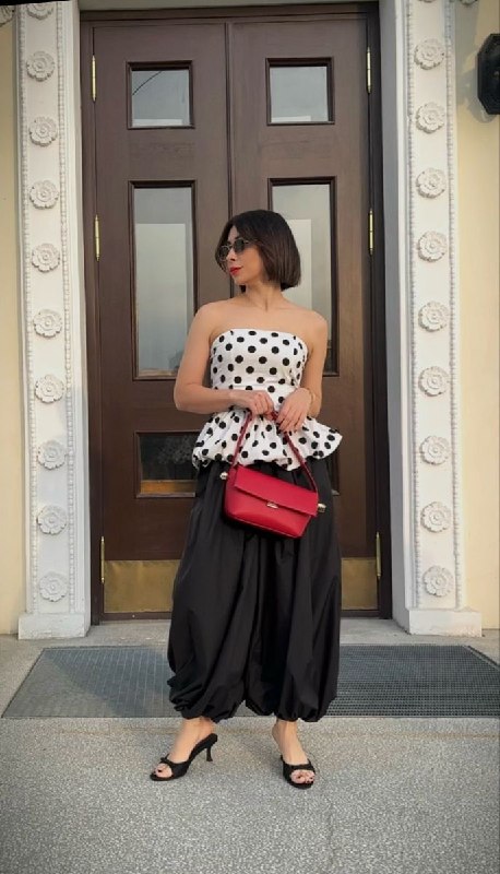 Городской снимок: женщина в белой баске в горох и свободной чёрной юбке, повседневный вариант с игривым акцентом на бедрах и талии.