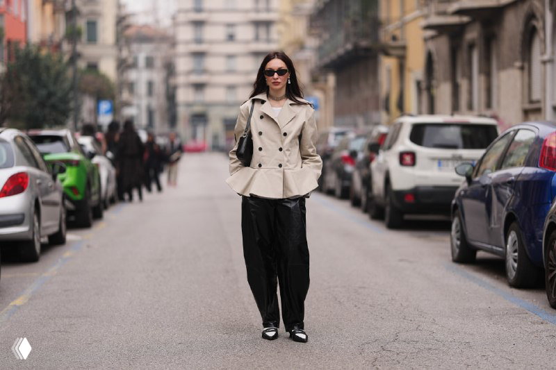 Уличный кадр: женщина в тренчe с расширенной баской, лёгкий городской образ, баска работает как декоративный и функциональный элемент формы.