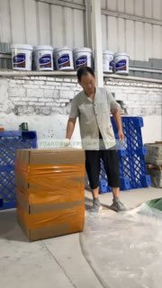 Сотрудник на складе оборачивает коробку защитной плёнкой и скотчем; на заднем плане видны упаковочные материалы, канистры и паллеты — этап упаковки BuyBox.