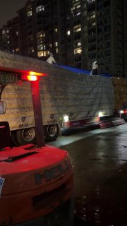 Грузовик с закрытым тентом на территории склада ночью, виден погрузчик и высотные здания; сцена транспортировки товаров BuyBox в Китае.