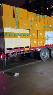 Крупный план прицепа с жёлтыми коробками и видимым логотипом BuyBox во время разгрузки на складе в Китае в тёмное время суток.
