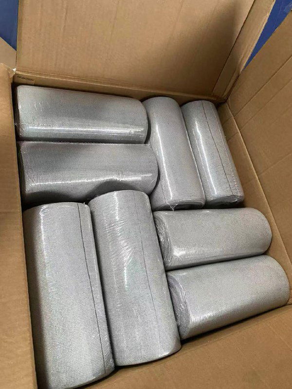 Открытая картонная коробка с серыми свернутыми салфетками/рулонами внутри; видно текстуру и плотную укладку каждого рулона для оптовой отправки.