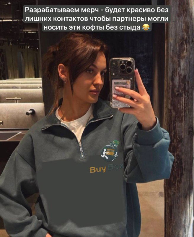 Селфи девушки в зеркале в тёмной толстовке с логотипом BuyBox: кадр иллюстрирует идею мерча и ожидания команды по корпоративному стилю.