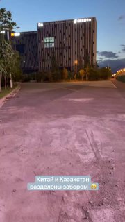 Фасад современного здания или бизнес-центра вечером: пустая стоянка и подсветка на фоне сумерек, остановка вблизи логистического хаба.