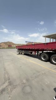 Пустой прицеп и часть площадки логистического терминала при ярком солнце: сцена разгрузки/ожидания для грузовиков без людей рядом.