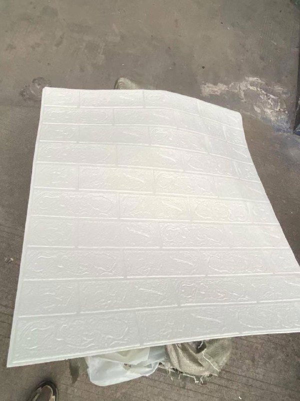 Одна белая самоклеящаяся панель с тиснением, лежащая на рабочем полу; видно фактуру и размер элемента для отделки интерьера.