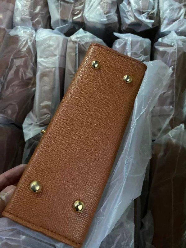 Вид снизу коричневой сумки: металлические ножки, швы и текстура материала на фоне упаковки — демонстрация качества и конструкции изделия.