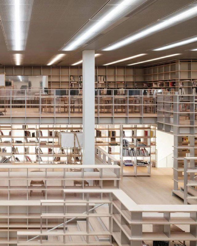 Просторная библиотечная зона с деревянными стеллажами и открытыми балконами — минималистичный дизайн и много света в интерьере проекта.