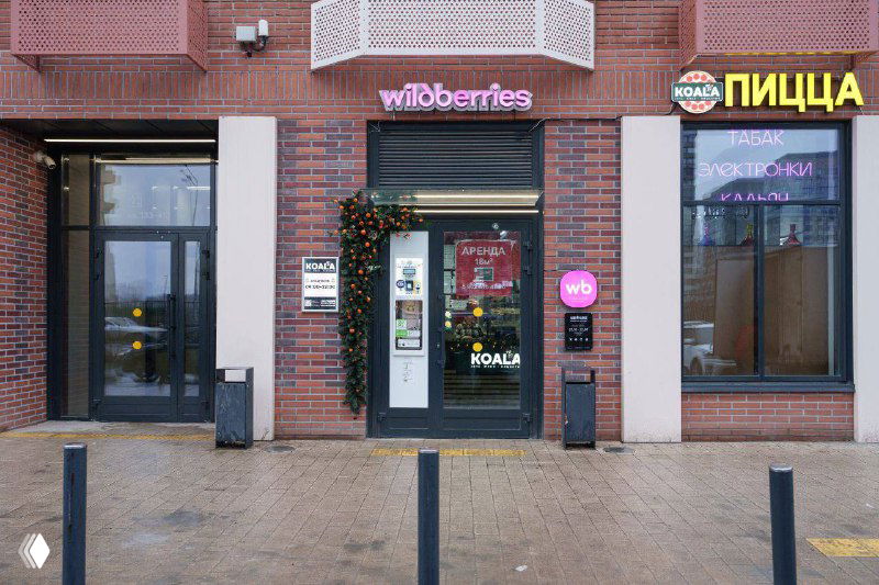 Фасад входа в пункт выдачи Wildberries: вывеска с логотипом над дверью на фоне кирпичной облицовки, пример интеграции фирменного знака в городской фасад.