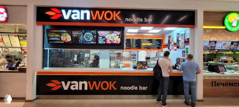 Торговая точка VanWok в фудкорте торгового центра: стойка с крупной вывеской VanWok, меню и посетители у прилавка.