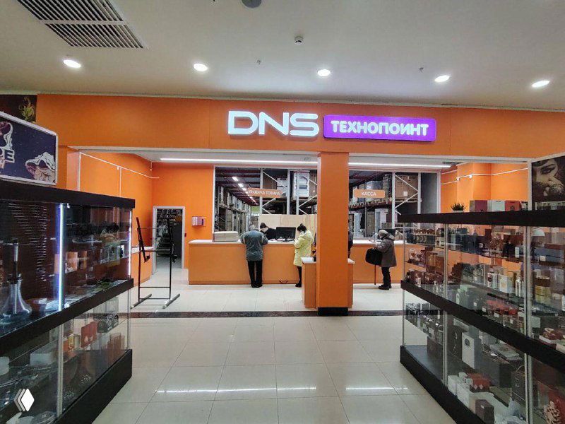 Фасад и зона выдачи DNS TechnoPoint: оранжевый брендированный модуль с прилавком и витринами, где клиенты получают заказы.